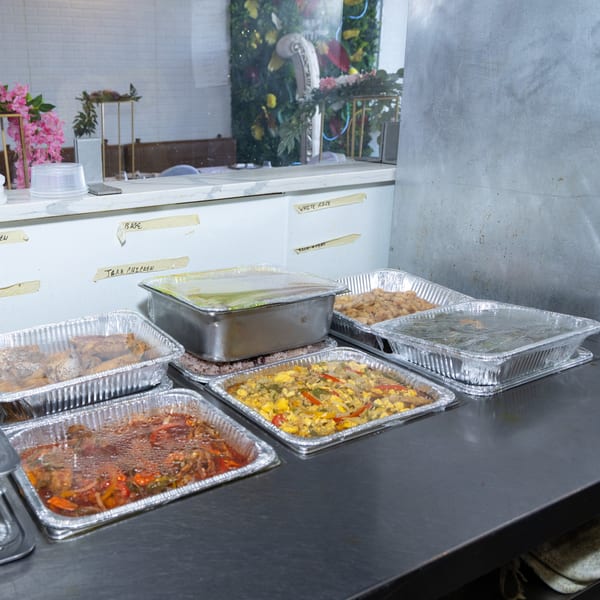 Multiple foil pans of Jamaican dishes like jerk chicken and rice, ready for serving.