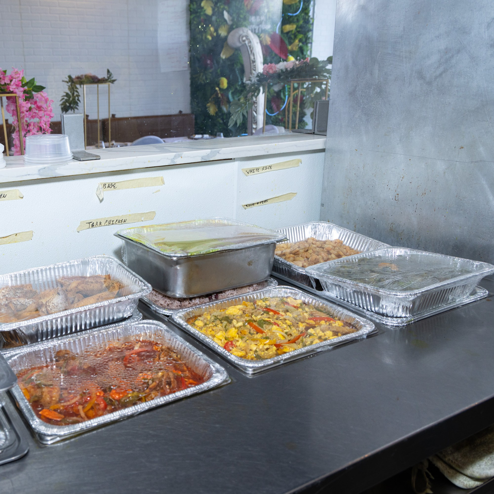 Multiple foil pans of Jamaican dishes like jerk chicken and rice, ready for serving.