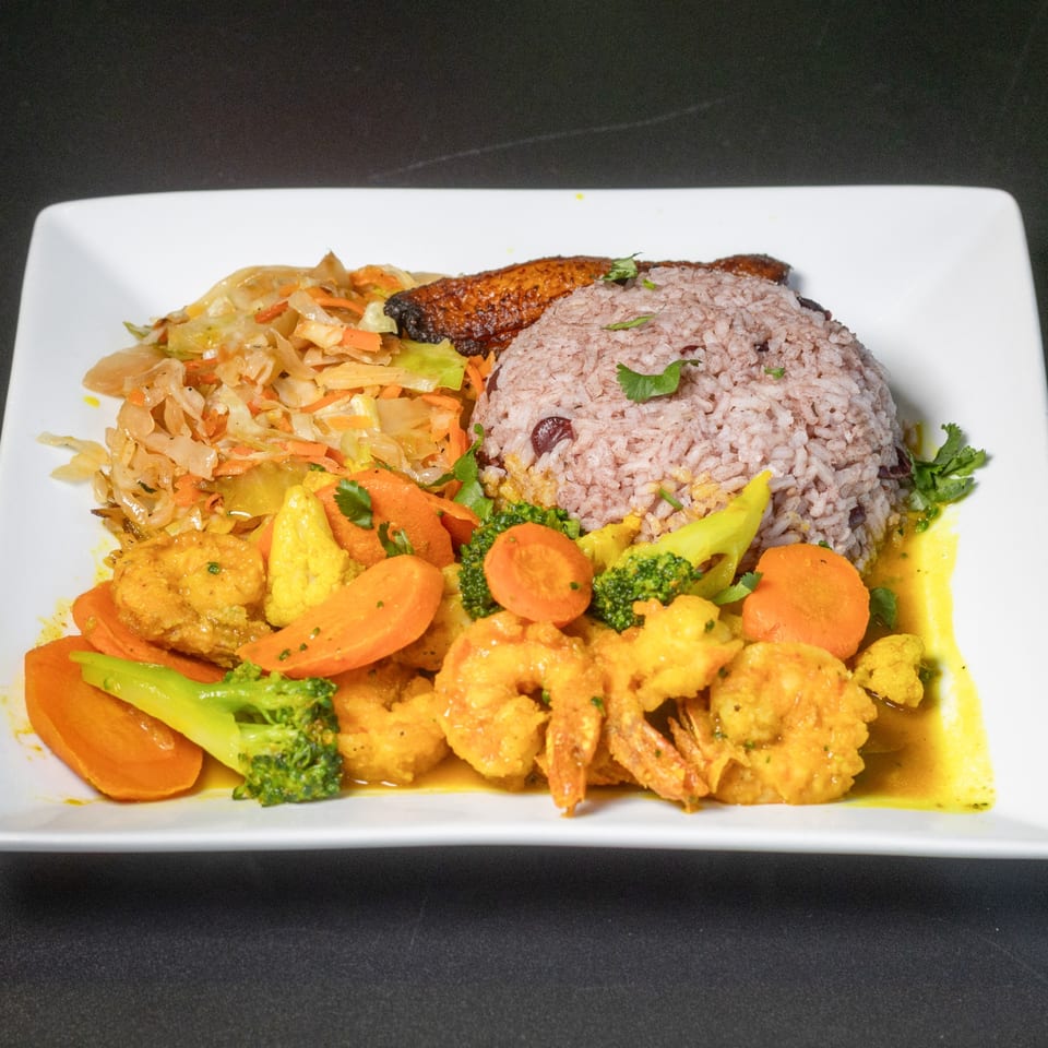 Curried shrimp with rice and peas, steamed cabbage, and plantain on a white plate.