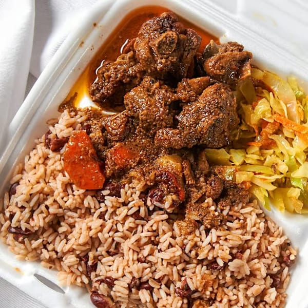 Curried goat with rice and peas, and steamed cabbage in a white takeout container.