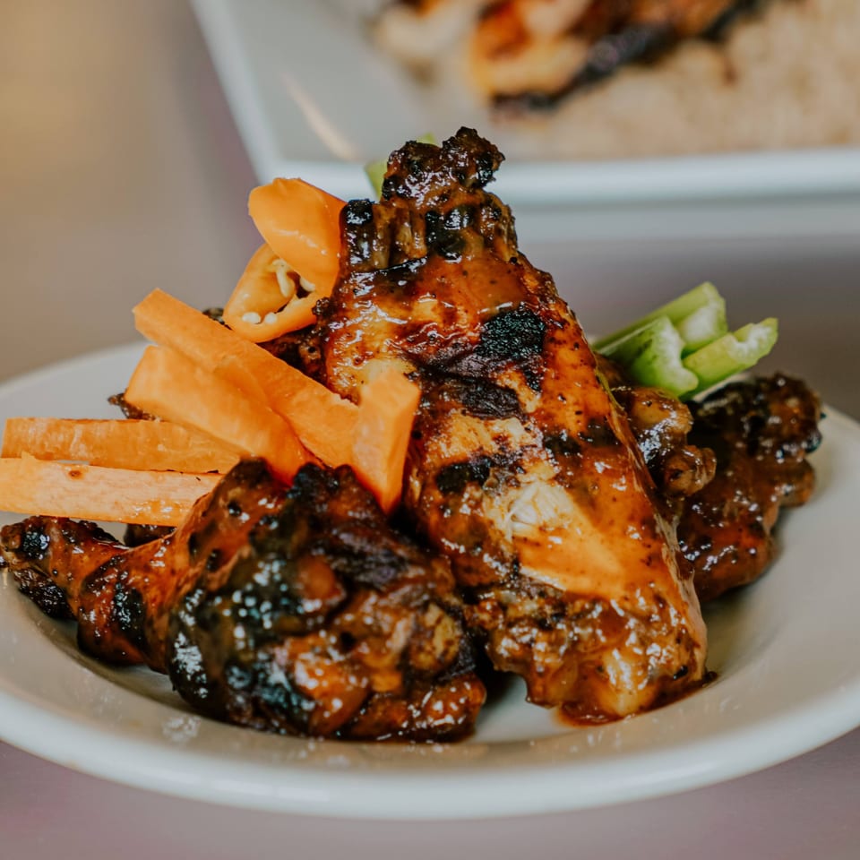 Jerk chicken wings with sweet potato fries and celery sticks on a white plate.