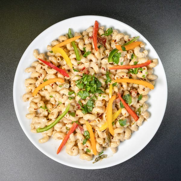 Creamy macaroni pasta with colorful bell peppers, red pepper flakes, and fresh parsley on a white plate.
