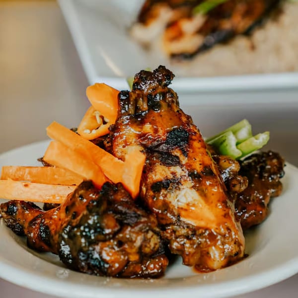Grilled chicken wings with sweet potato fries and green pepper slices on a white plate.
