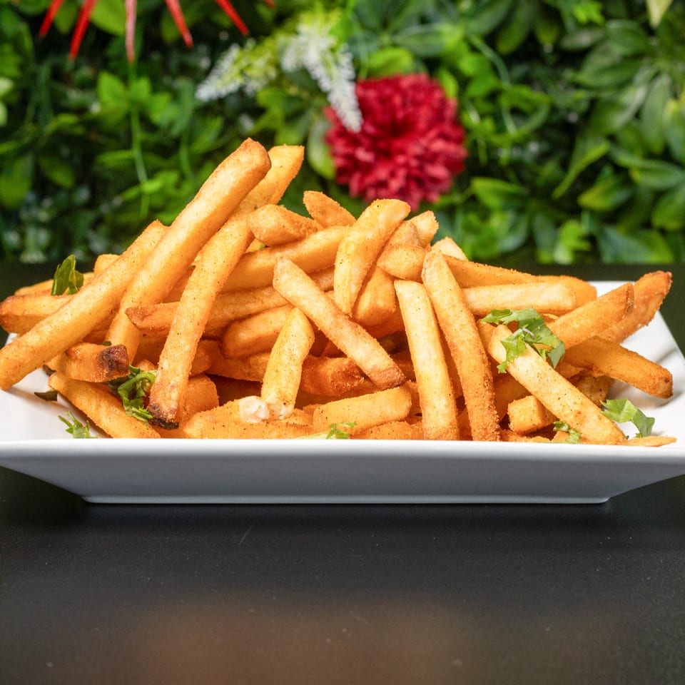 Crispy golden french fries seasoned with spices and garnished with fresh herbs on a white plate.