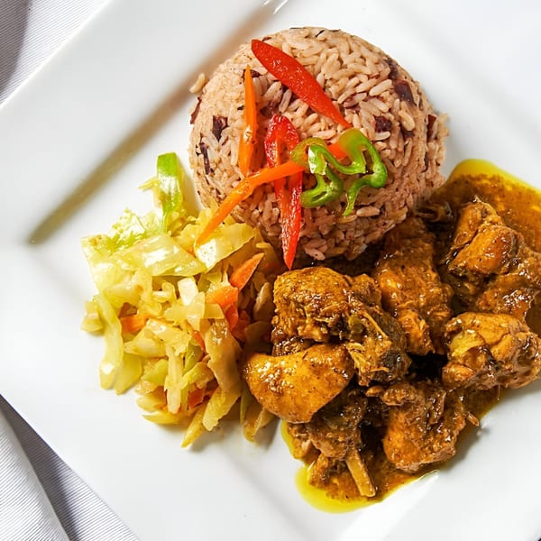 Jamerican Kitchen Cafe's curry chicken with rice and peas, and steamed cabbage on a white plate.