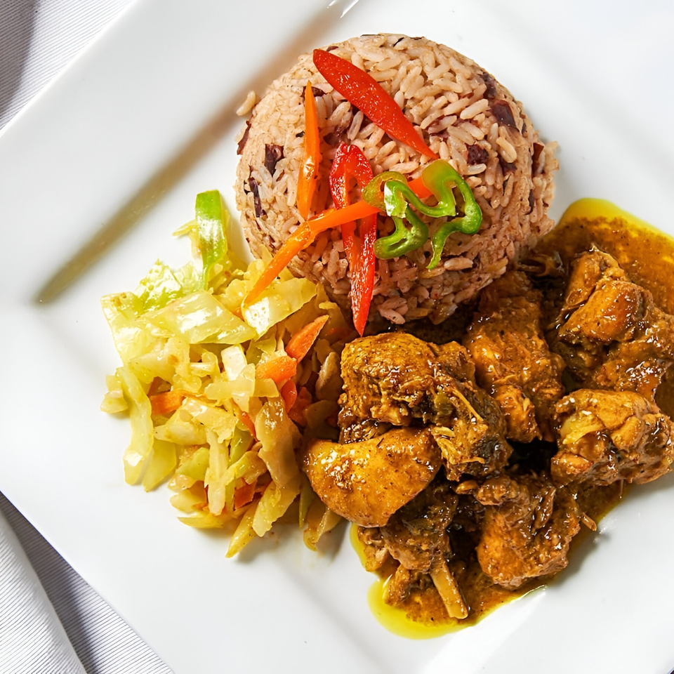Jamerican Kitchen Cafe's curry chicken with rice and peas, and steamed cabbage on a white plate.