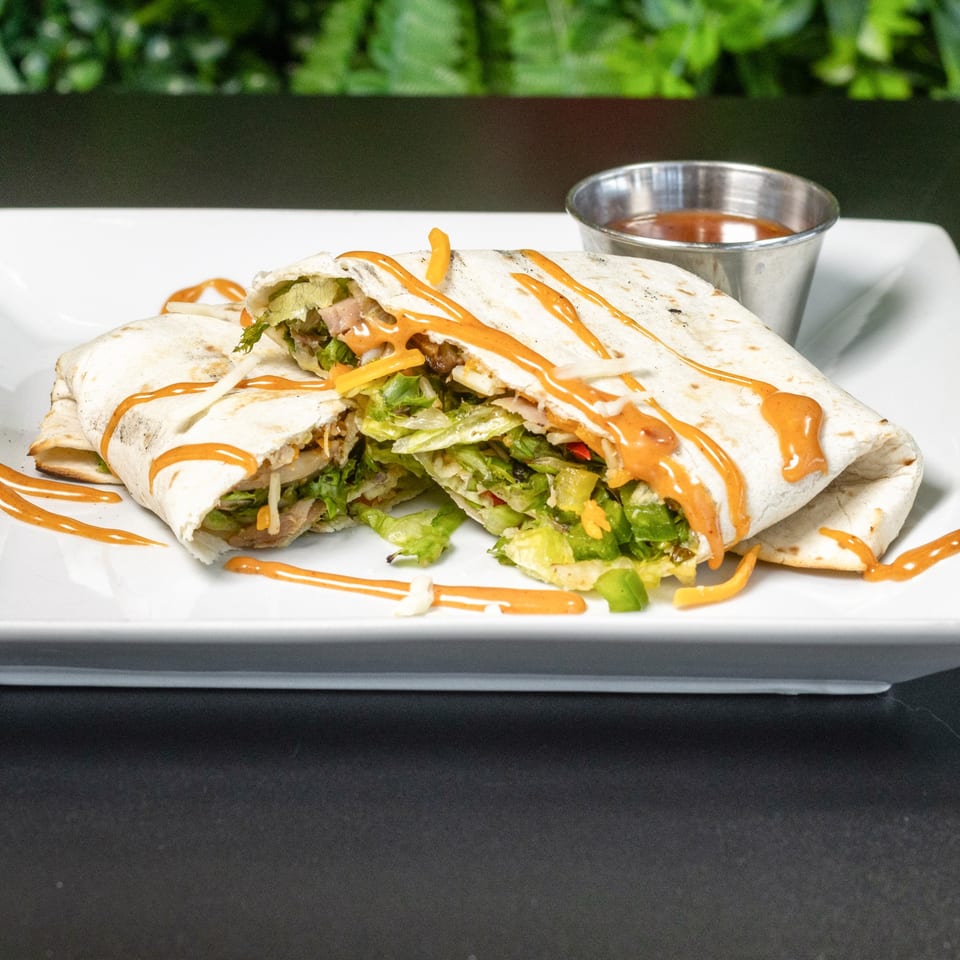 Two halves of a Jamerican Kitchen Cafe wrap, filled with lettuce and meat, drizzled with sauce.