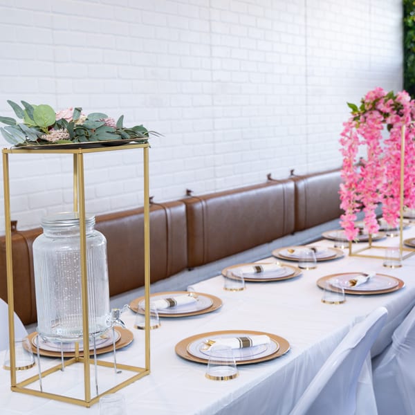 A long table set with gold-rimmed plates, glasses, and pink floral decorations at Jamerican Kitchen Cafe.