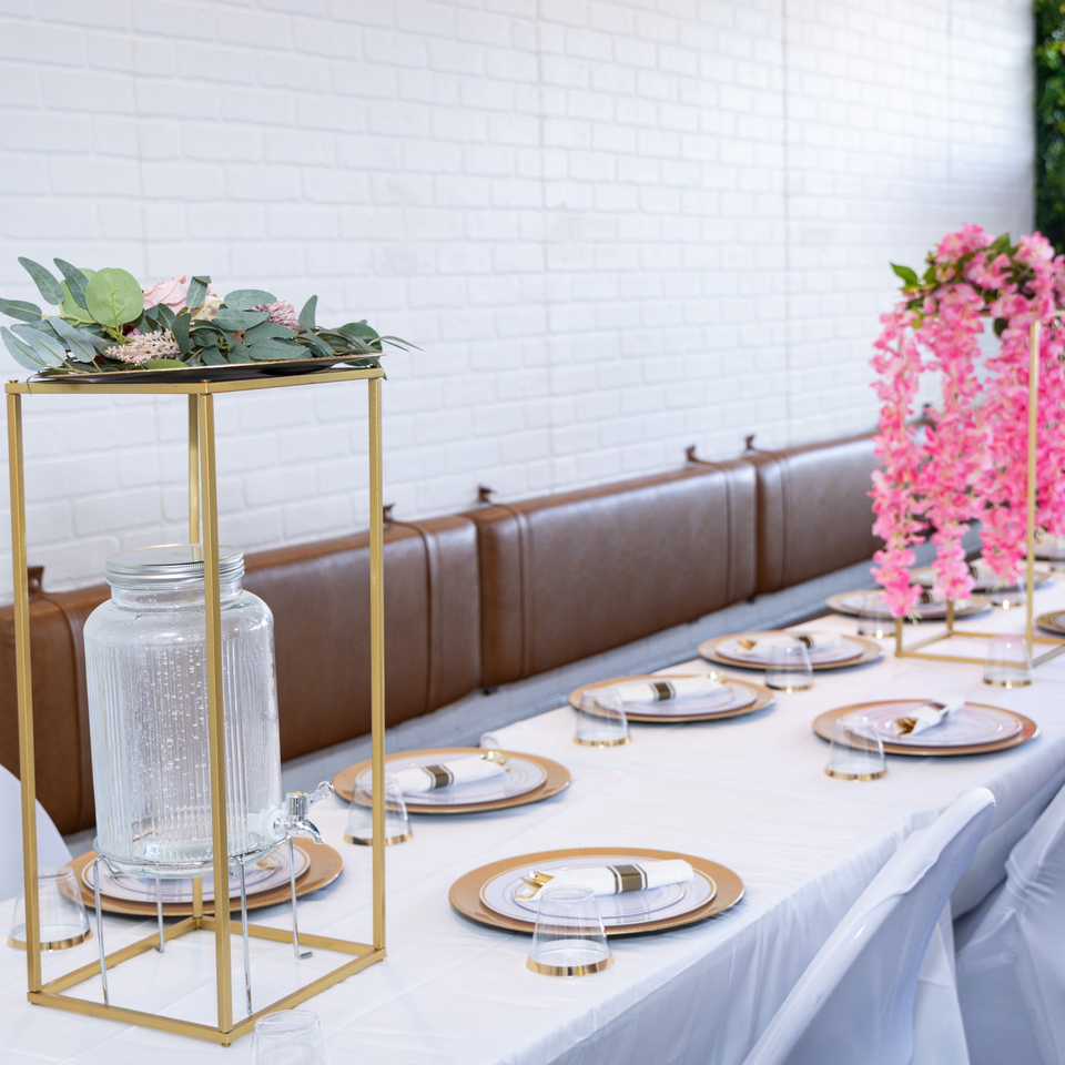 A long table set with gold-rimmed plates, glasses, and pink floral decorations at Jamerican Kitchen Cafe.