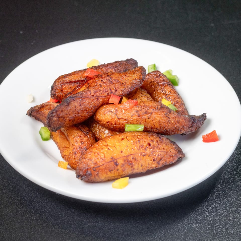A white plate filled with golden-brown fried plantains, garnished with diced colorful bell peppers.